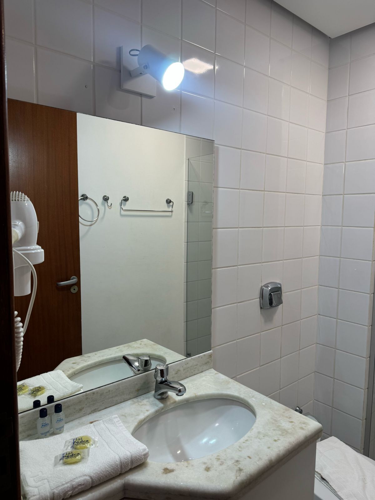 A bathroom with a sink, mirror, towel rack, and a hairdryer on a wall.