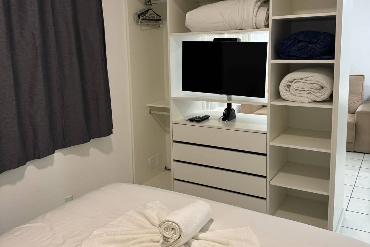 Een slaapkamer met een opgemaakt bed, een televisie op een standaard, en een inloopkast met planken en lades.