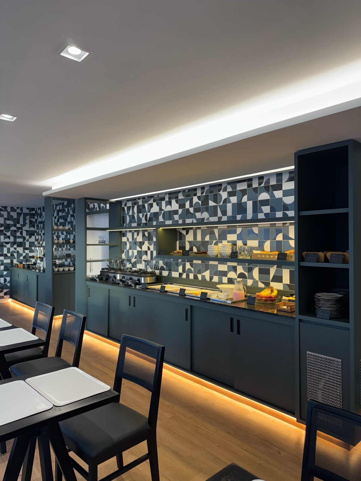 A modern kitchen with geometric patterned backsplash, built-in appliances, and a buffet area with food items.