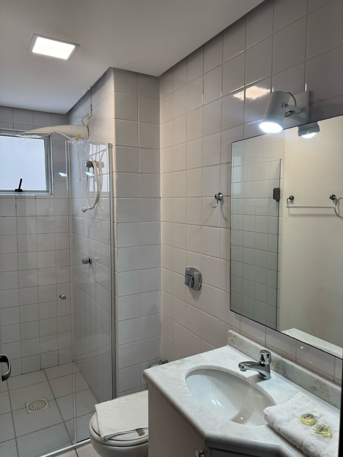 A modern bathroom with a glass shower enclosure, a toilet, a sink with a mirror, and a window.