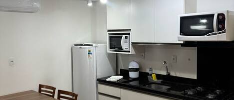 Una cocina compacta con una mesa de comedor, sillas, un refrigerador, un microondas, estufa y un lavabo.