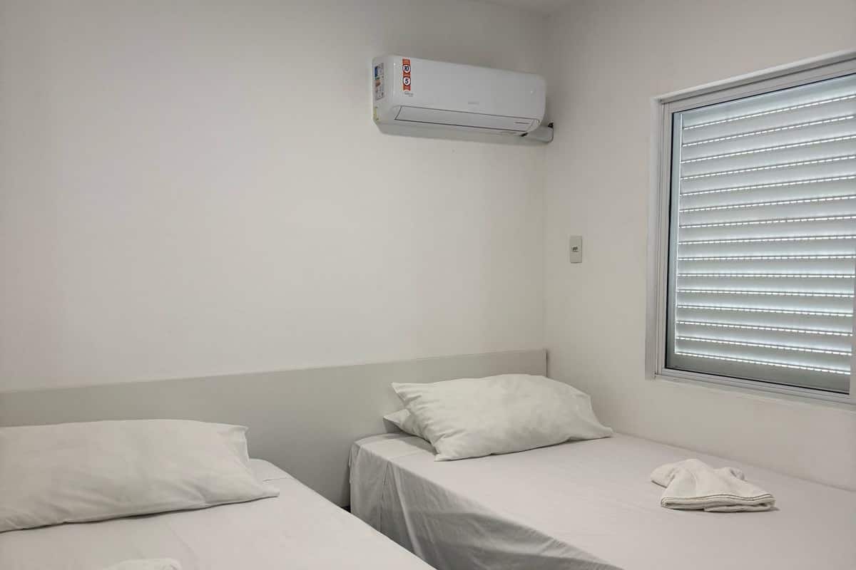 Een kleine, schone kamer met twee eenpersoonsbedden, een raam met zonwering, een airconditioning en een betegelde vloer.