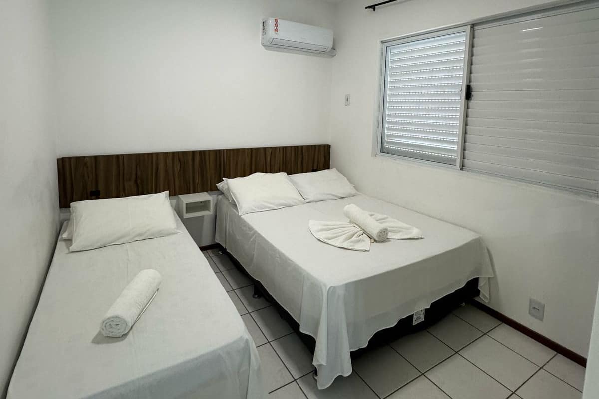 Een kleine, schone kamer met twee eenpersoonsbedden, een raam met zonwering, een plafondlamp en een airconditioning.