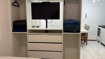 Ein Schlafzimmer mit Fernseher auf einem Schrank, einem Kleiderschrank mit mehreren Einlegeböden und einem Essbereich mit Tisch und Stühlen.
