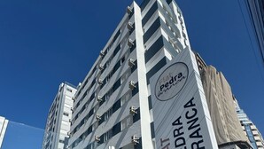 Ένα σύγχρονο κτίριο με μια πινακίδα που αναγράφει «Flat Pedra Branca», υποδεικνύοντας ότι πρόκειται για ξενοδοχείο ή συγκρότημα κατοικιών.