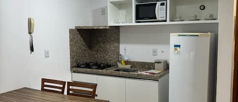 A compact kitchen with white cabinets, a granite countertop, a microwave, a refrigerator, and a dining table with chairs.