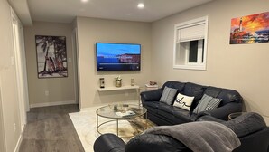 A modern living room with a black leather sofa, a glass coffee table, and a flat-screen TV mounted on the wall.