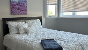 A bedroom with a large bed, a window with blinds, and a painting on the wall.