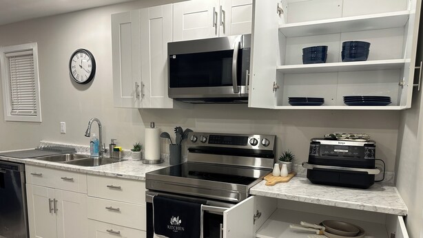 A modern kitchen with white cabinets, stainless steel appliances, a microwave, oven, and a dishwasher.