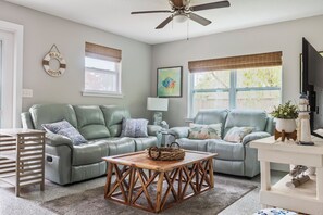 Ein Wohnzimmer mit zwei grünen Ledersofas, einem Holztisch, einem Deckenventilator und einem Fernseher.