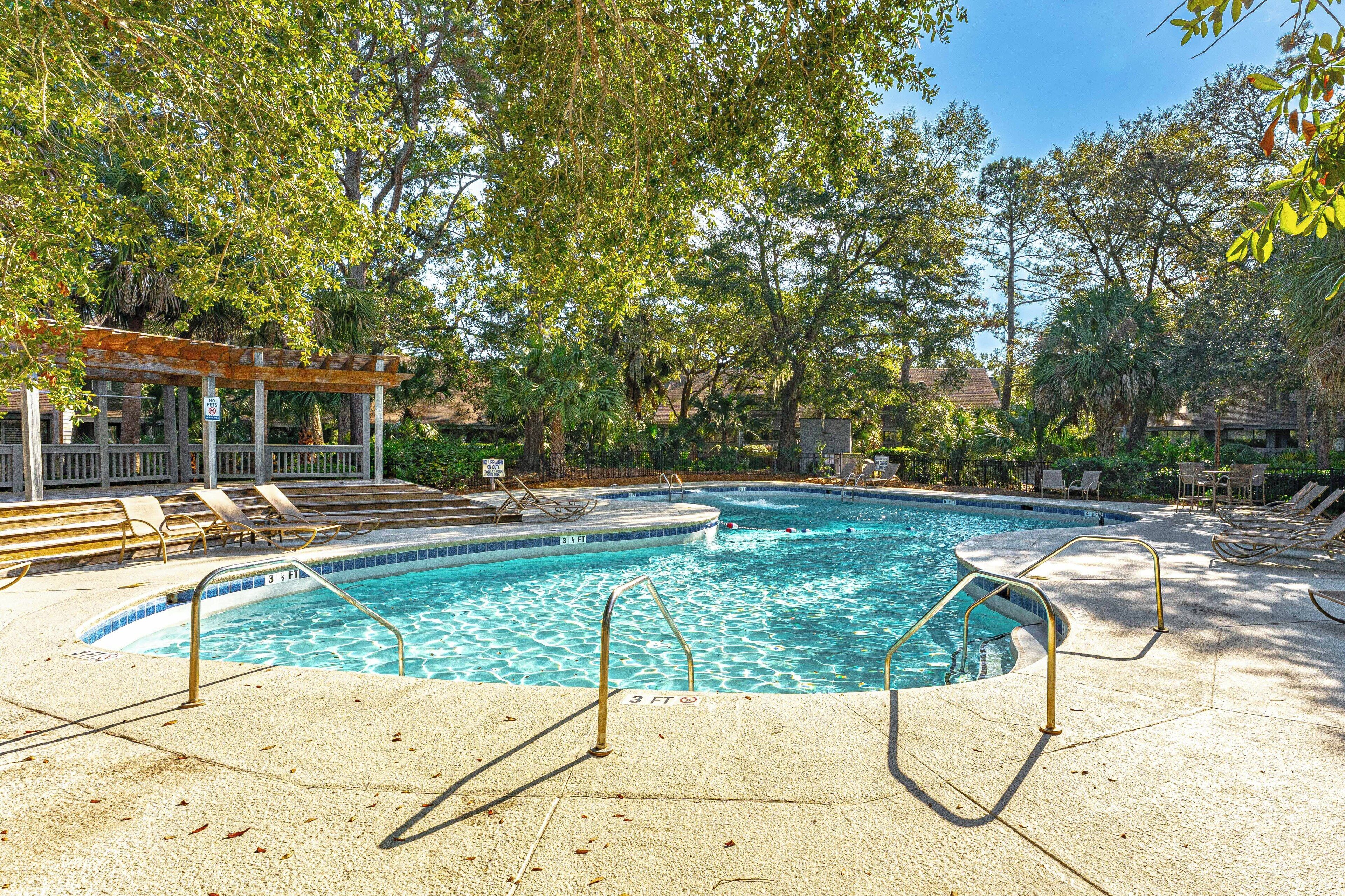 A swimming pool with a wooden deck and lounge chairs, surrounded by trees.