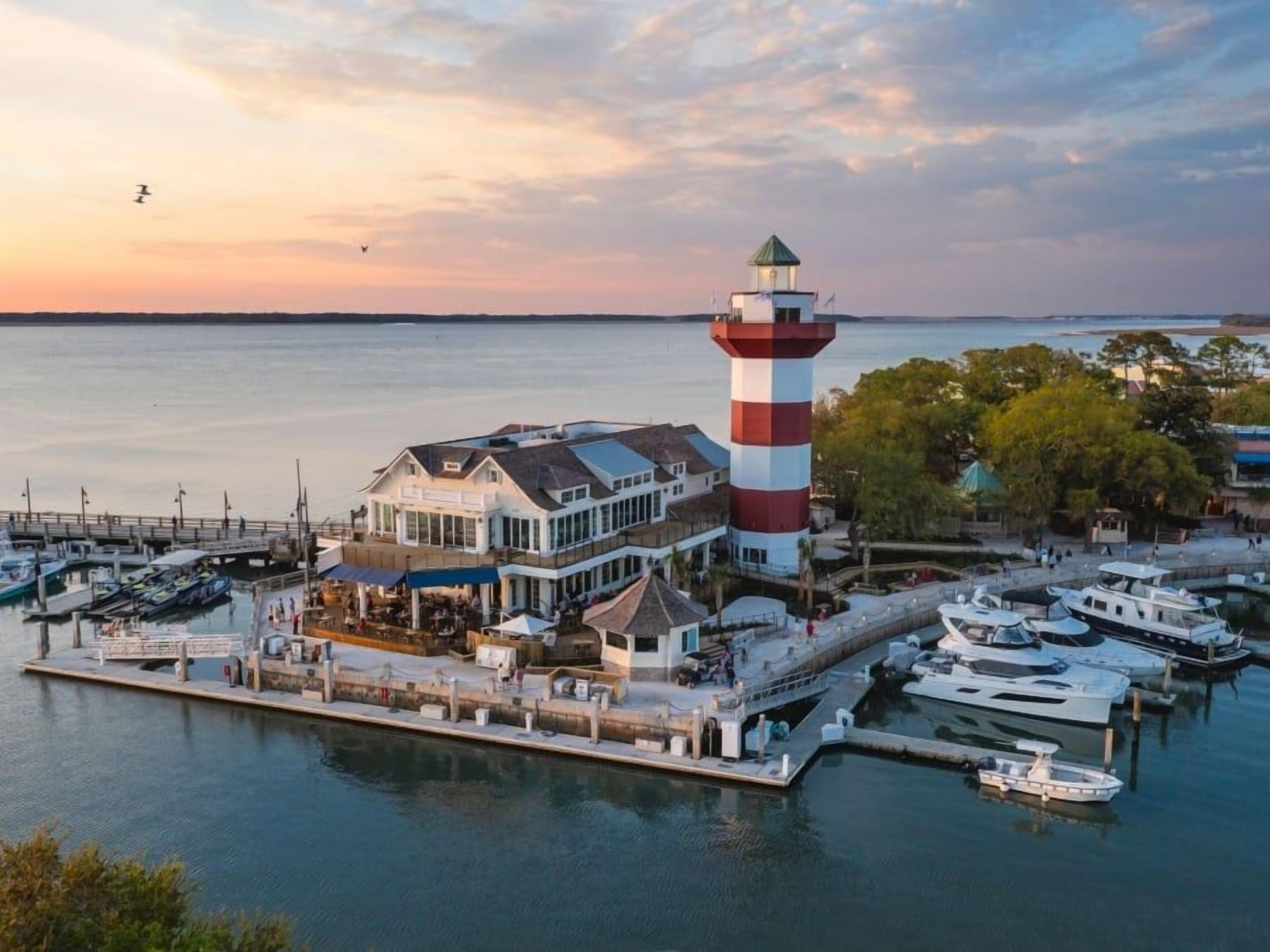 A waterfront property with a lighthouse, docked boats, and a building with a balcony overlooking the water.