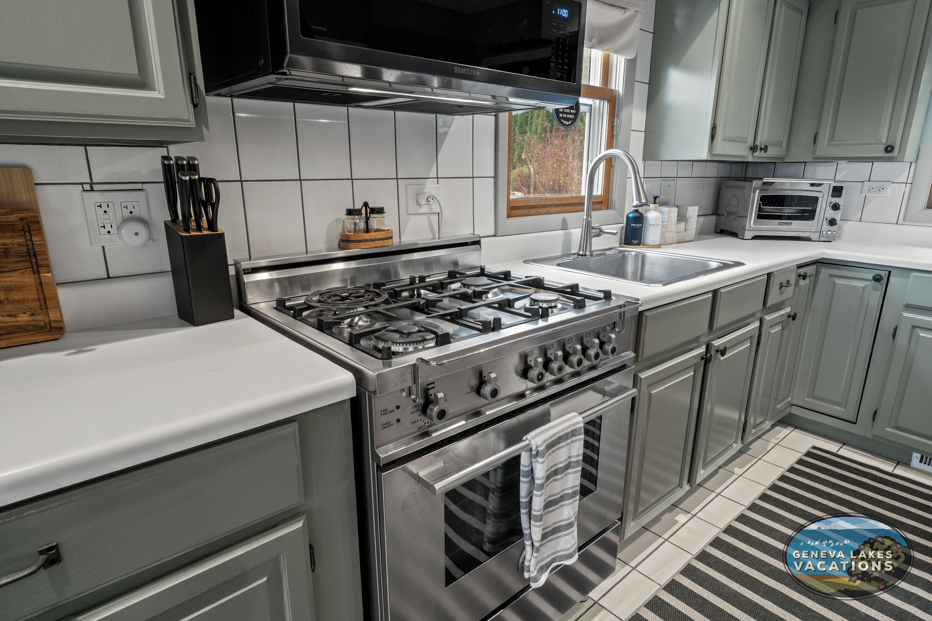 A modern kitchen with stainless steel appliances, white countertops, and light grey cabinets.