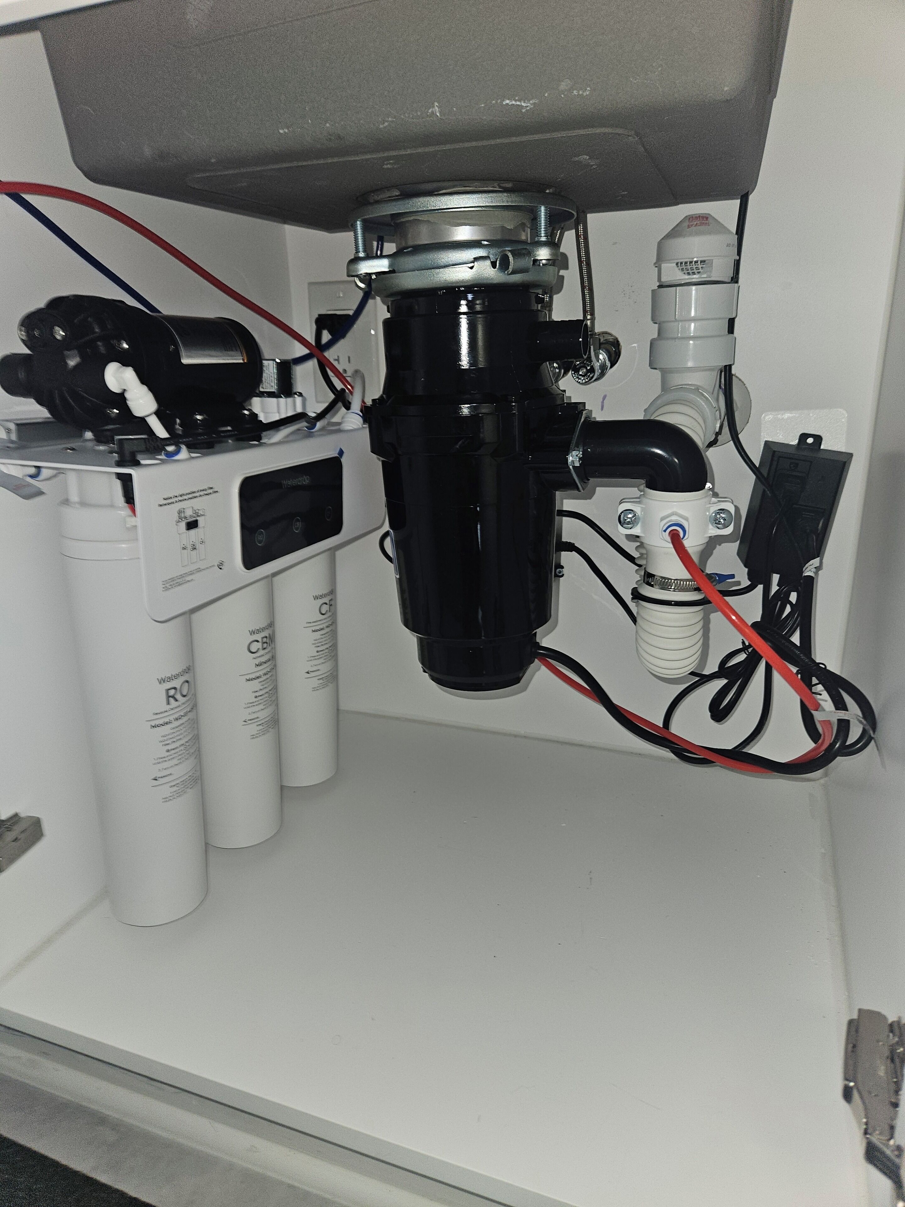 A water filtration system with multiple components and hoses, including a pump and a filter unit, connected to a white wall.