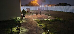 An outdoor patio with a brick floor, two chairs, a table, and potted plants.
