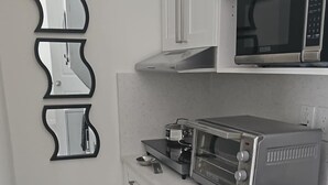 Een keuken met witte kastjes, een magnetron, een broodrooster en een bijzondere spiegel aan de wand.