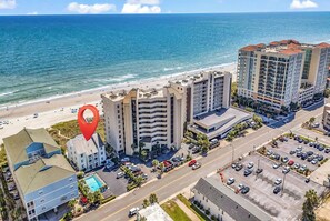 Un hotel costero con varias edificaciones, un estacionamiento y una playa al fondo.