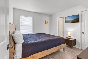 Un dormitorio con cama, mesita de noche, lámpara y una puerta que da a otra habitación.