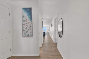 A hallway with white walls, wooden flooring, and a large abstract painting on the left wall. - Direct Oceanfront w/ Private Balcony (North Myrtle Beach)