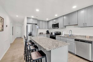 A modern kitchen with grey cabinets, a stainless steel refrigerator, a microwave, a coffee maker, and a dishwasher. - Direct Oceanfront w/ Private Balcony (North Myrtle Beach)