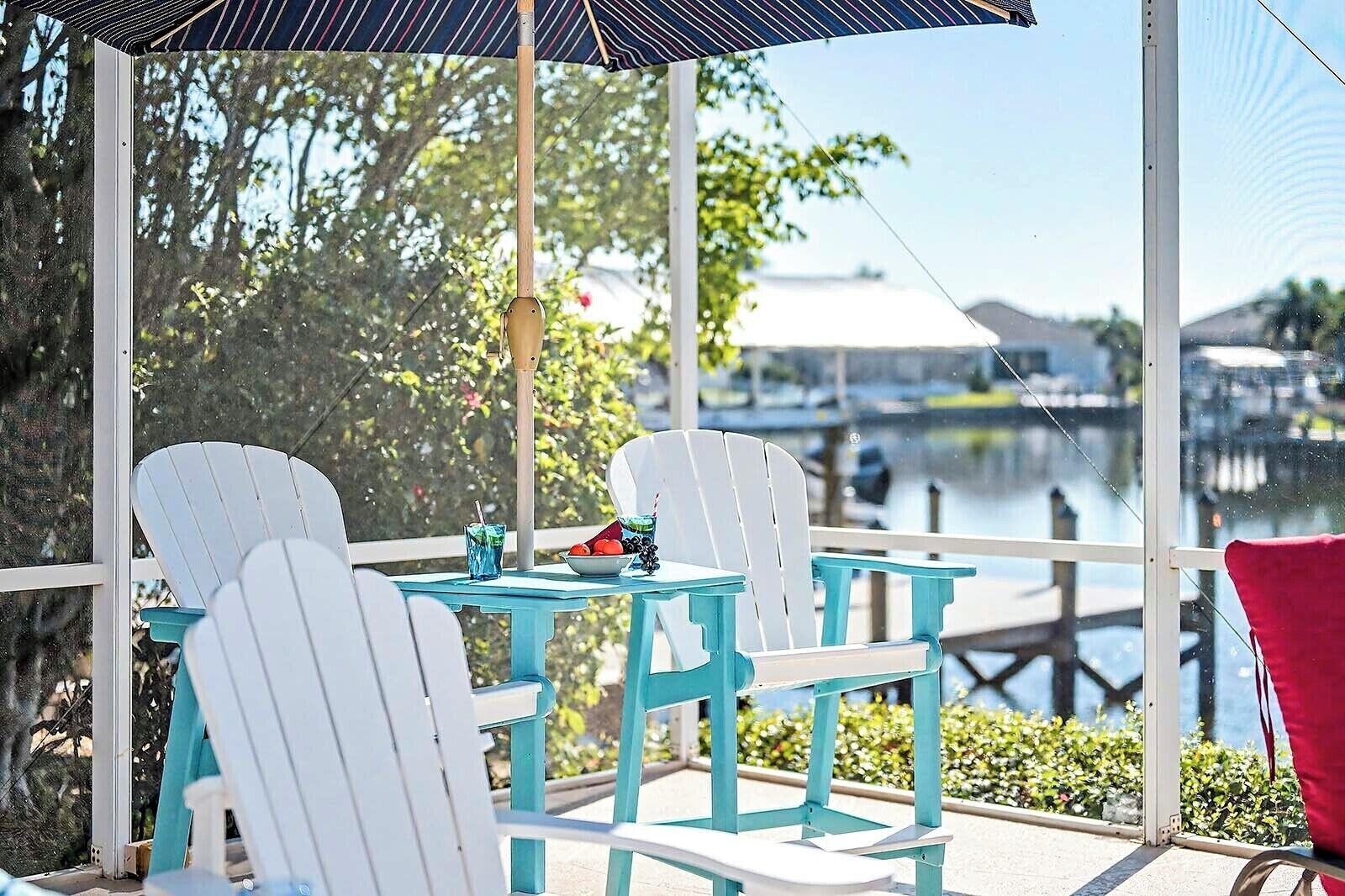 Un espacio de estar al aire libre cubierto con sillas Adirondack blancas y turquesas, una mesa y una bebida.