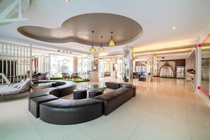 A spacious lobby with a modern design, featuring a large seating area with sofas and a coffee table, a glass partition, and a ceiling with a unique curved design. - Sunday JA Plus Hotel (Pattaya)