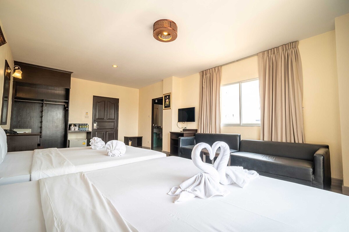 A hotel room with two beds, a sofa, a television, and a minibar.