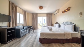 A hotel room with a large bed, a sofa, a TV, and a view of the city. - Sunday JA Plus Hotel (Pattaya)