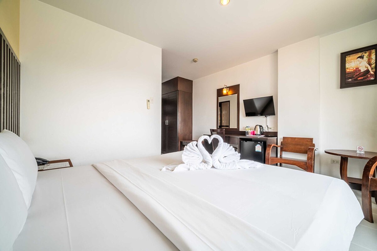 A hotel room with a neatly made bed, a desk with a chair, a small table, and a television on the wall.