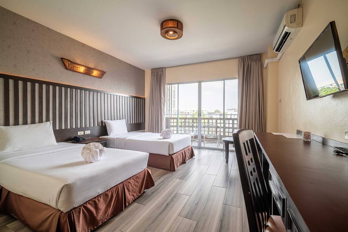 A hotel room with two beds, a desk, a chair, a TV, and a balcony with curtains.