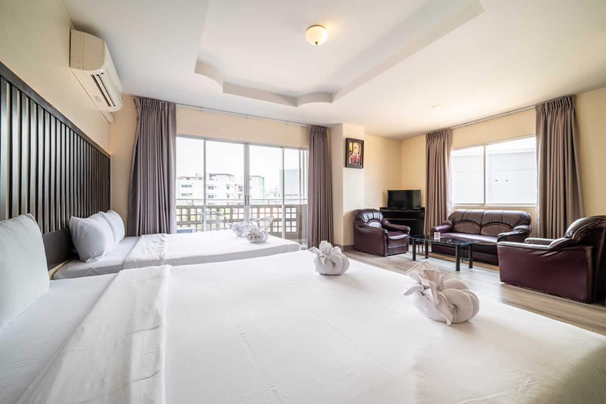 A hotel room with two beds, a sofa, a TV, and a balcony with a view of buildings.