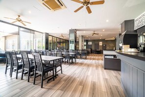 A spacious restaurant with high ceilings, multiple ceiling fans, and a central island with a coffee machine. Tables and chairs are arranged for dining. - Sunday JA Plus Hotel (Pattaya)