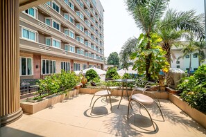 A hotel courtyard with outdoor seating, palm trees, and a multi-story building with balconies. - Sunday JA Plus Hotel (Pattaya)