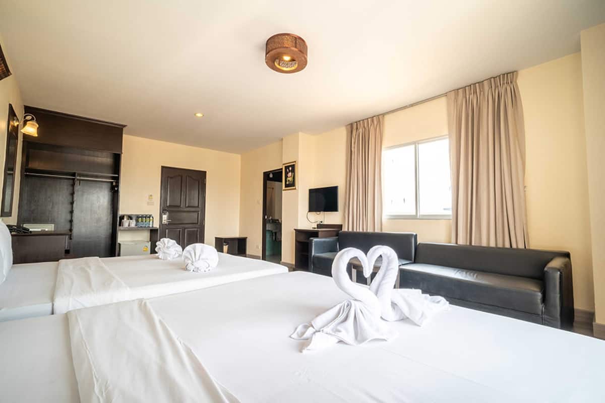 A hotel room with two beds, a sofa, a television, and a minibar.
