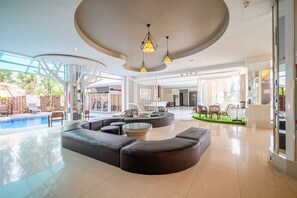 A spacious lobby with a curved seating area, a pool, and large windows. - Sunday JA Plus Hotel (Pattaya)