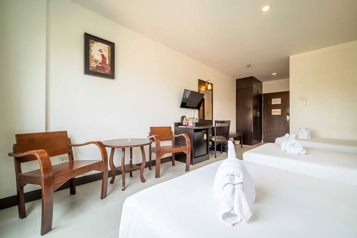 A hotel room with two beds, a desk, a chair, a small table, and a television.