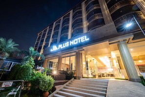A Plus Hotel with a modern architectural design, featuring a prominent entrance with steps leading up to the main doors, surrounded by lush greenery and palm trees. - Sunday JA Plus Hotel (Pattaya)