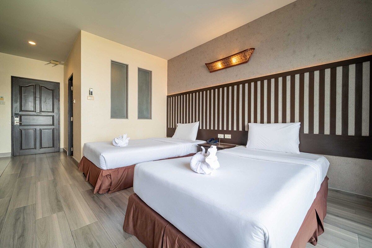 A hotel room with two beds, a wooden headboard, a wall-mounted light fixture, and a door.