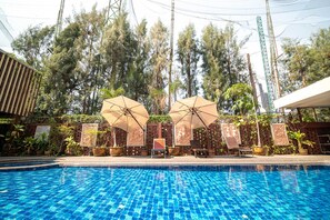 A swimming pool with tiled blue water, surrounded by lounge chairs and umbrellas, with trees and a building in the background. - Sunday JA Plus Hotel (Pattaya)