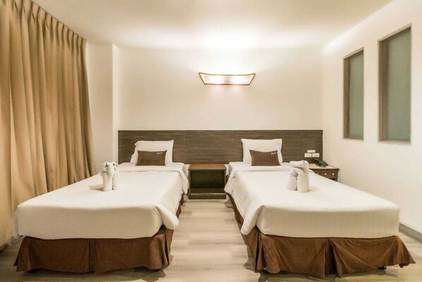 A hotel room with two beds, a wooden headboard, a small table, a nightstand, and a window. - Sunday JA Plus Hotel (Pattaya)