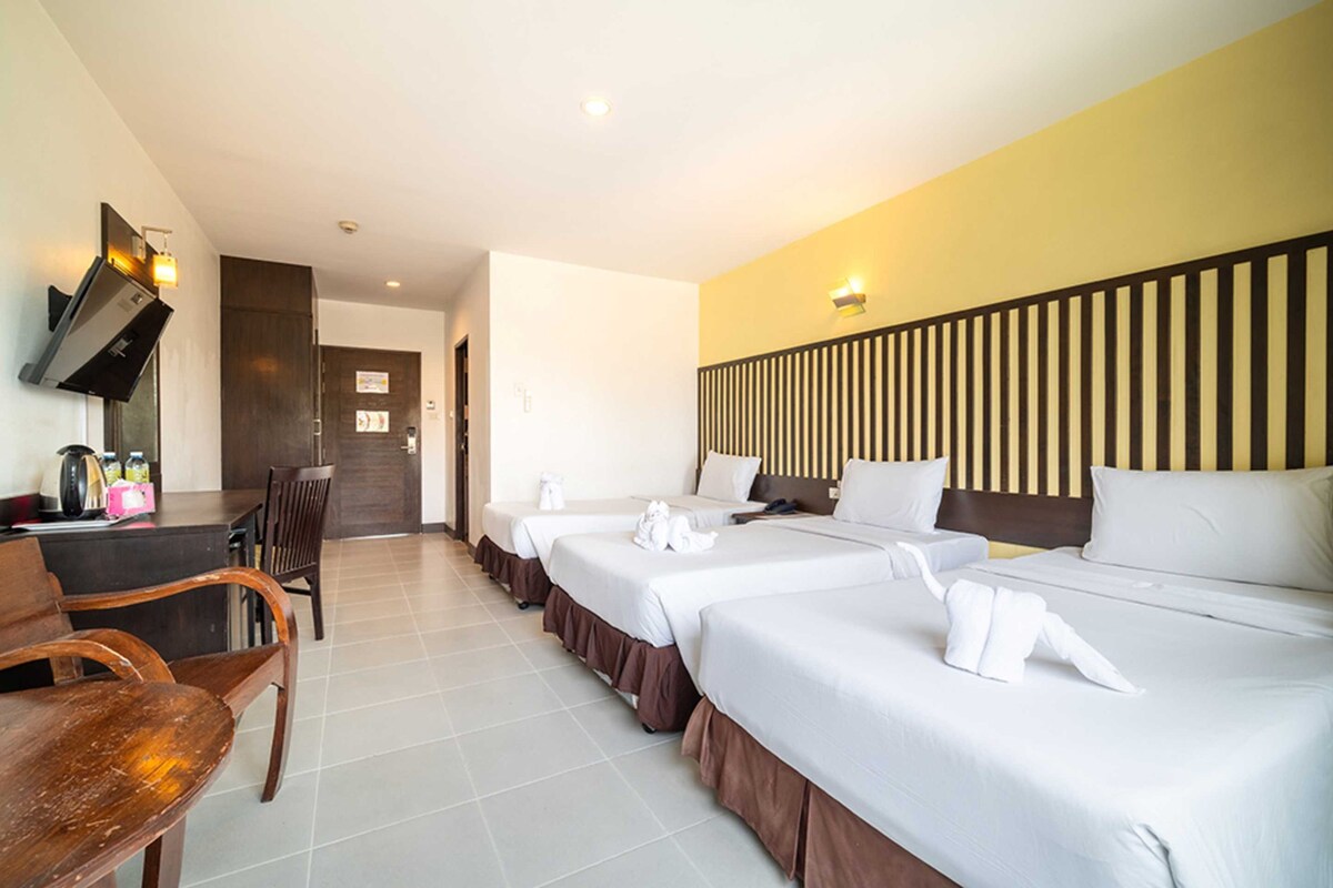 A hotel room with three beds, a wooden desk, and a dining area.