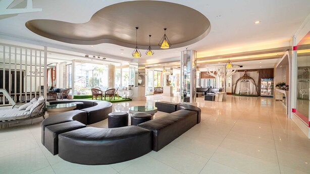 A spacious lobby with a modern design, featuring a large seating area with sofas and a coffee table, a glass partition, and a ceiling with a unique curved design. - Sunday JA Plus Hotel (Pattaya)