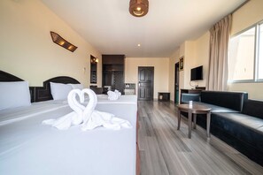 A hotel room with two beds, a sofa, a small table, a TV, and a kitchenette in the background. - Sunday JA Plus Hotel (Pattaya)