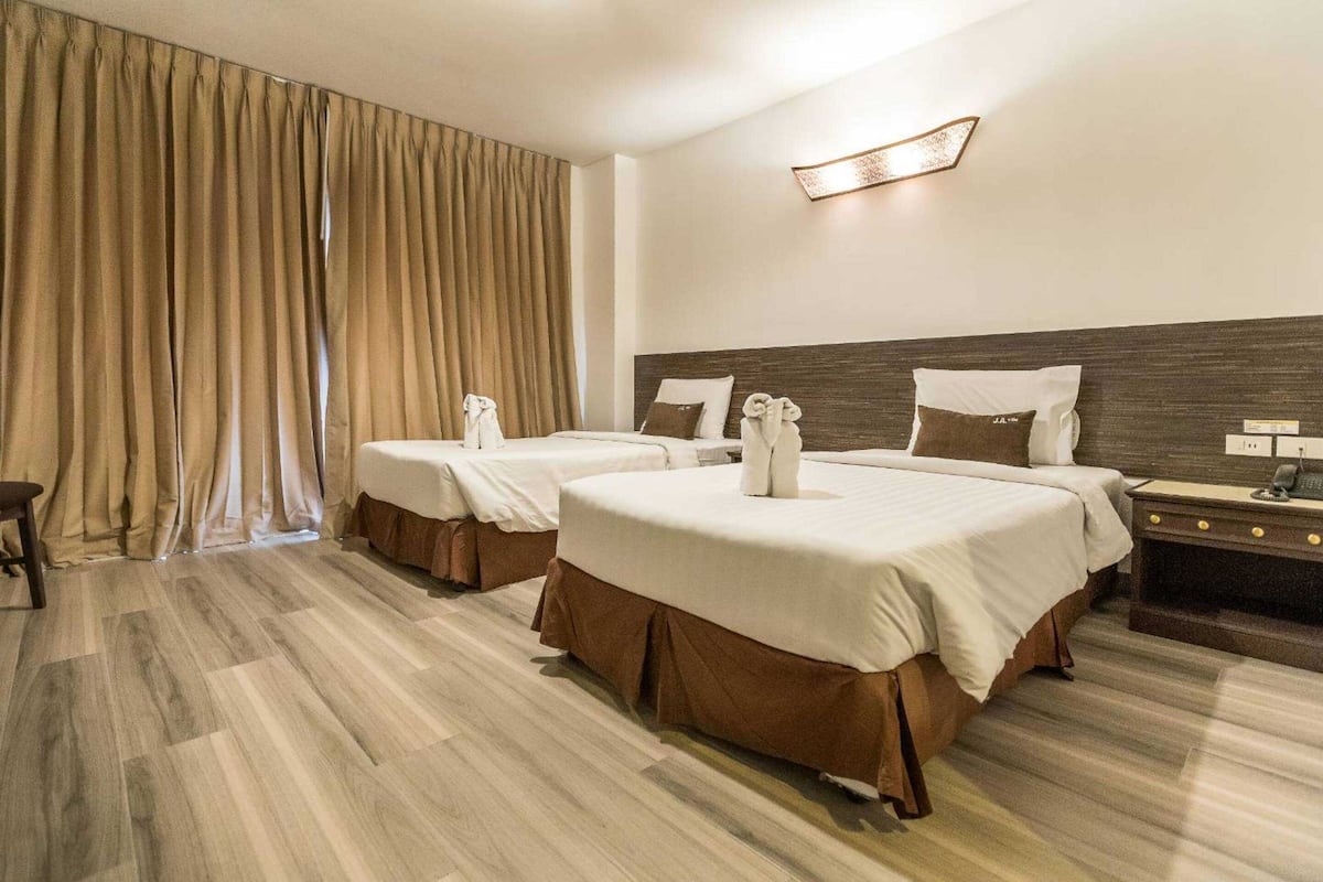 A hotel room with two beds, a nightstand, and a large window with curtains.