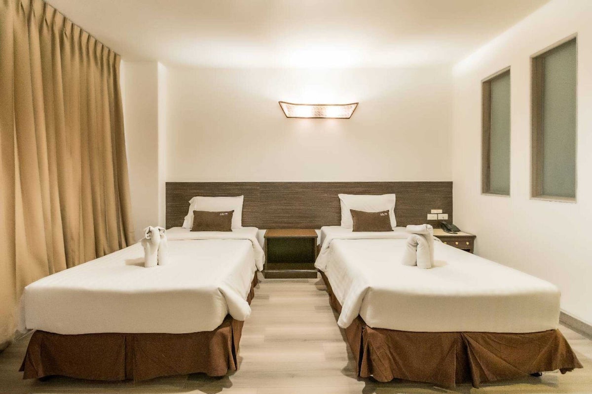 A hotel room with two beds, a wooden headboard, a small table, a nightstand, and a window.