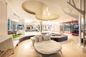 A modern hotel lobby with a central seating area, a large bed, and a Thai travel agency sign. - Sunday JA Plus Hotel (Pattaya)