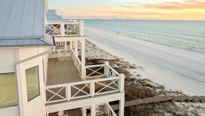 A beachfront property with a wooden deck and a balcony overlooking the beach.
