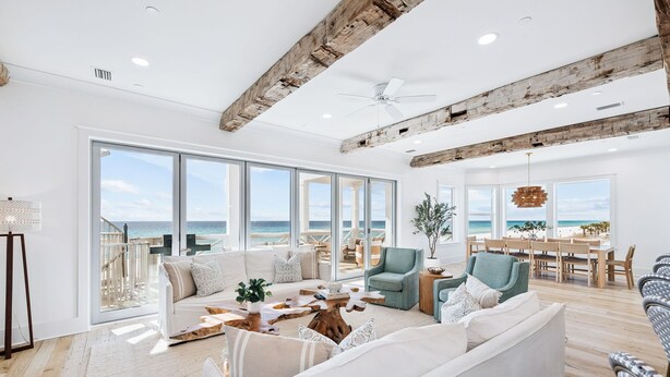 A spacious living room with a large window overlooking the ocean, wooden beams on the ceiling, and a cozy seating area with a coffee table.