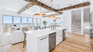 A spacious kitchen with a large island, wooden beams, and a view of the ocean.