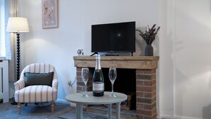 Una sala de estar con chimenea, televisor, un sillón a rayas y una mesa con dos copas de vino y una botella.